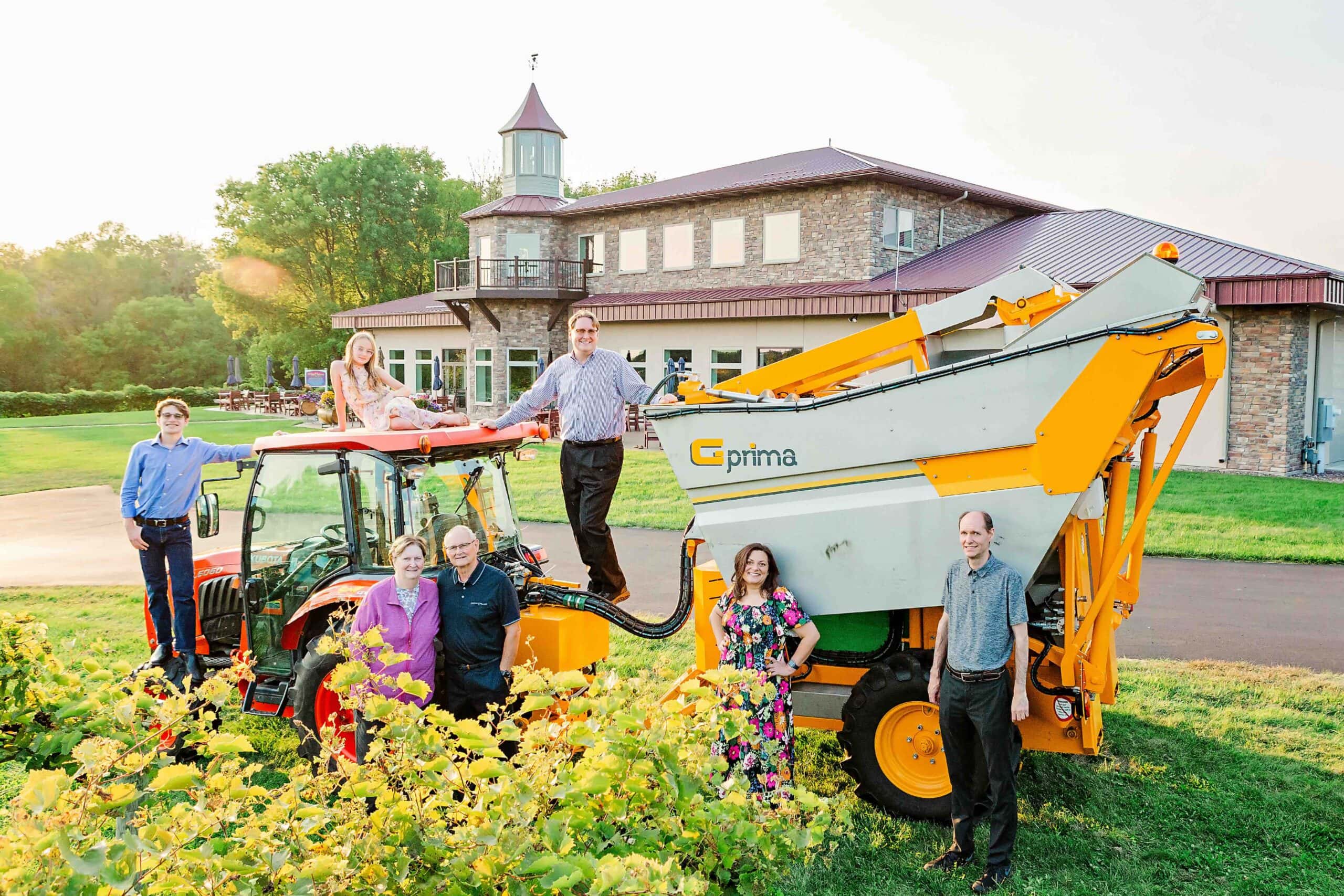 The Peterson family of Winehaven winery standing among Winehaven's tractor and harvesting equipment.  Grapevines are in the foreground and the Winehaven estate is in the background.