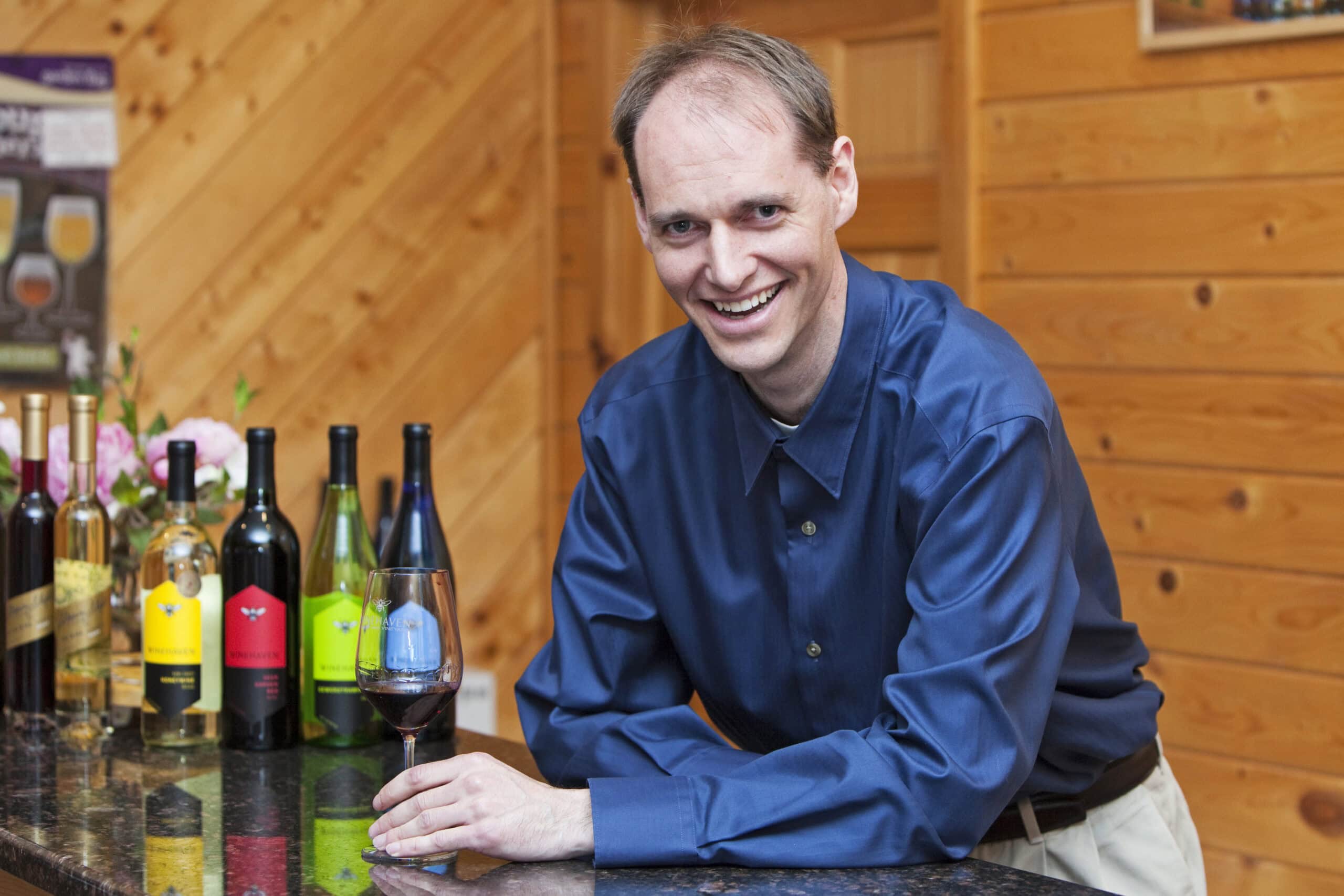 Troy Peterson of Winehaven winery holding a glass of red wine leaning on a surface with four bottles of wine on the surface.