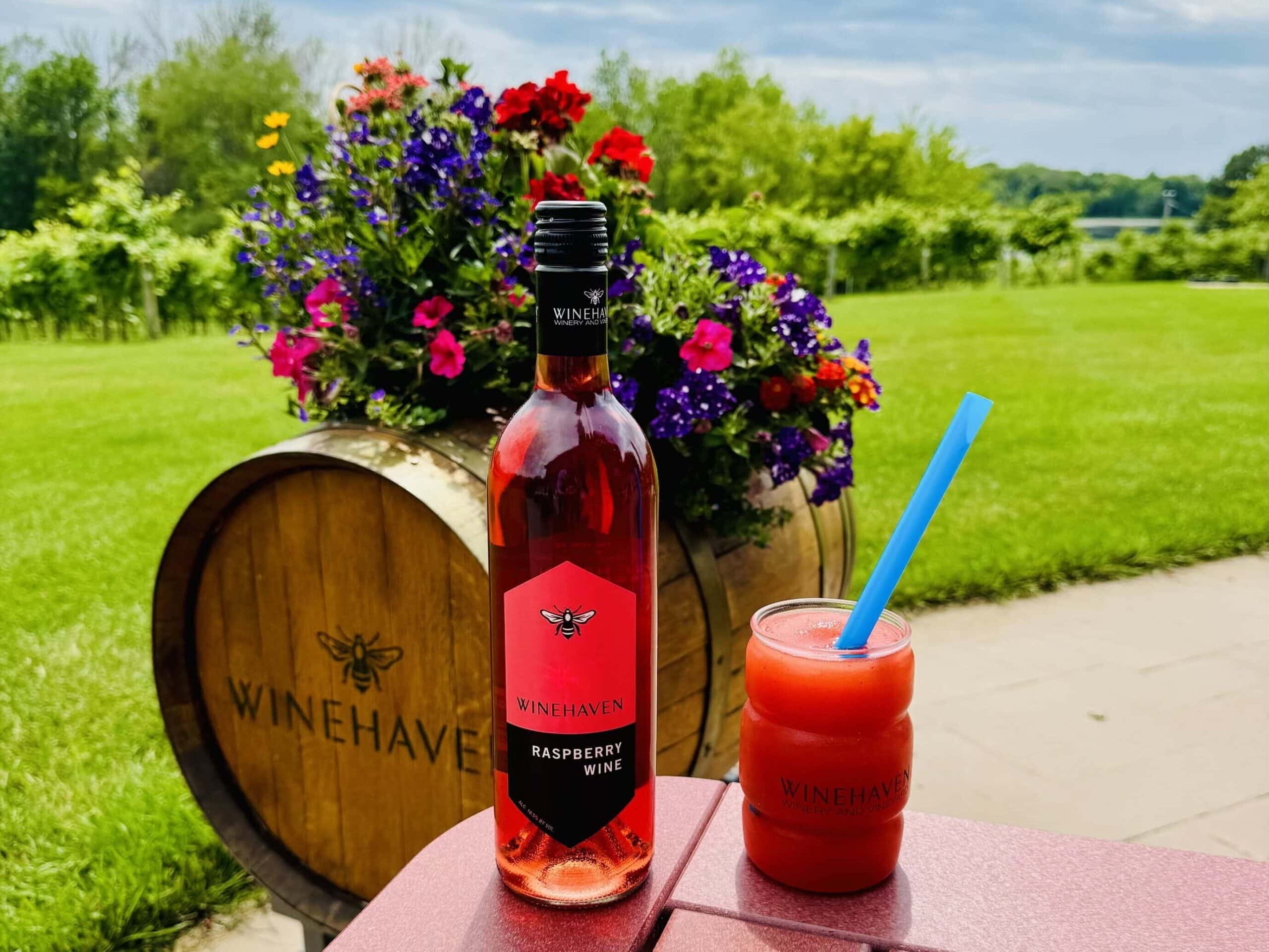 Winehaven Raspberry Wine and Raspberry Wine Slushy on patio in front of vines and wine barrel.